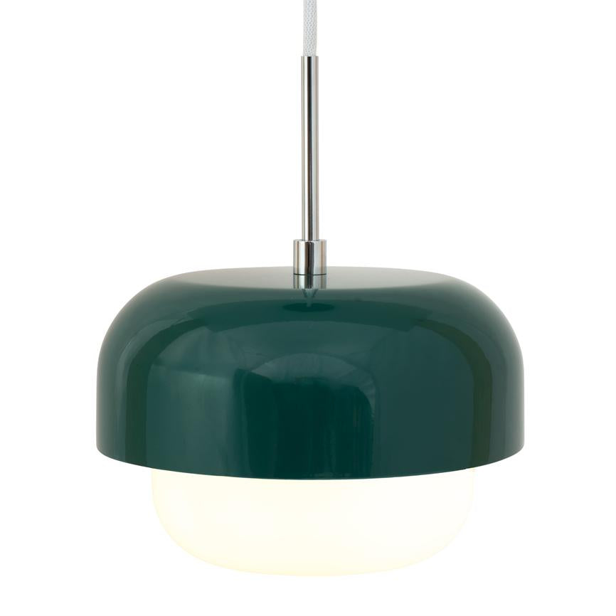 En grøn, blank pendellampe hænger i en kromstang og udsender blødt, varmt lys fra en hvid rund diffuser mod en neutral hvid baggrund.